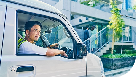 白い配達車両を運転する配達パートナーの横顔、住宅街の背景