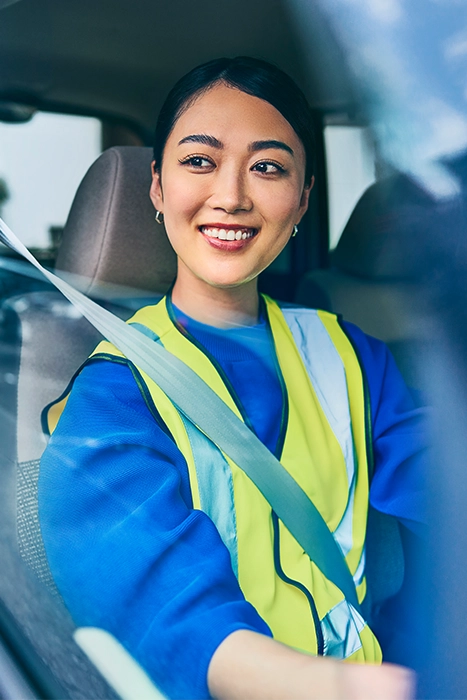 青いシャツと安全ベストを着た配達ドライバーが車の中で笑顔を見せている