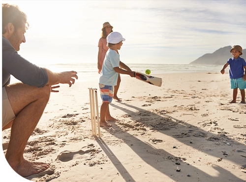 Family playing beach cricket at sunset