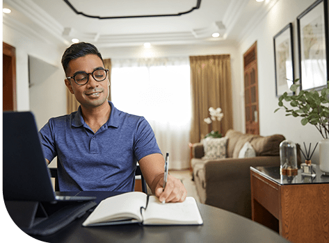Person writing in notebook from modern home office setup