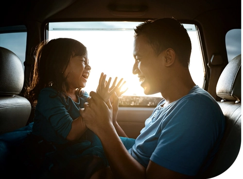 Parent and child playing patty-cake game in car backseat during sunset