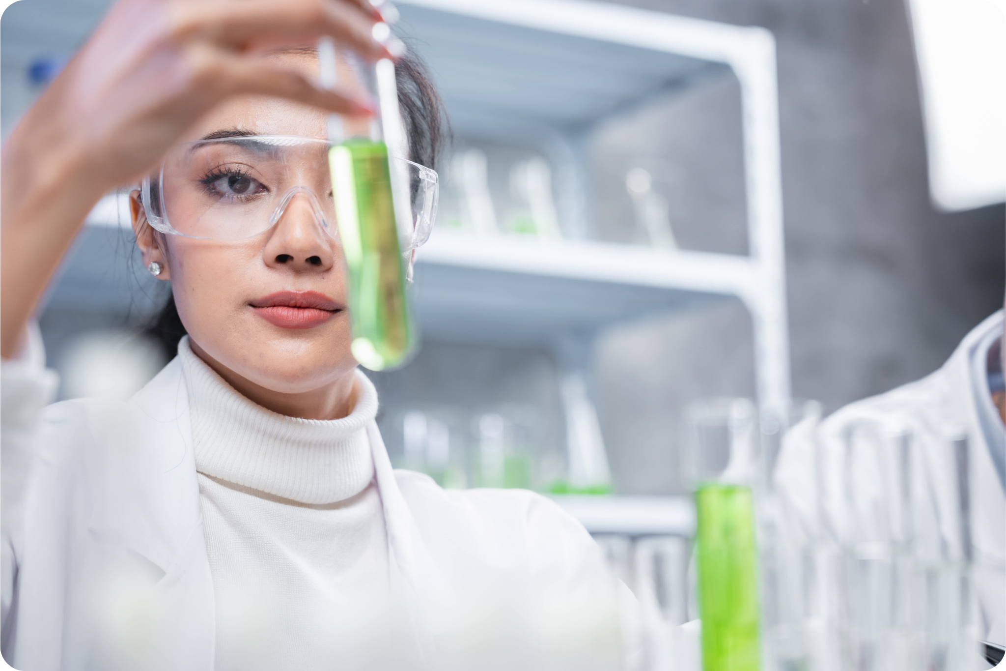 Mulher com óculos de proteção segurando tubo de ensaio com líquido verde em laboratório
