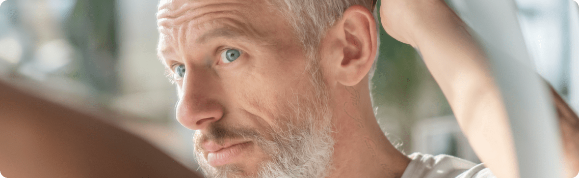 Man with thinning hair looks at receding hairline in mirror