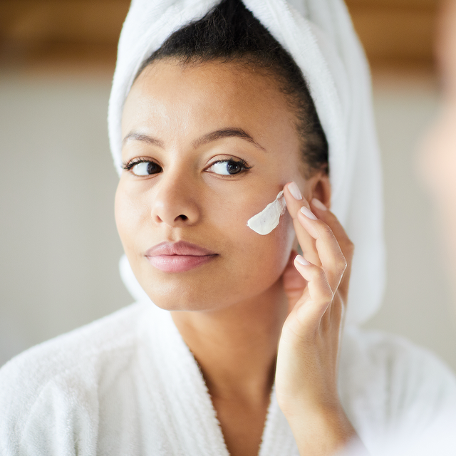 What causes dark spots? Woman in bathrobe applies dark spot corrector cream for facial melasma to her cheek