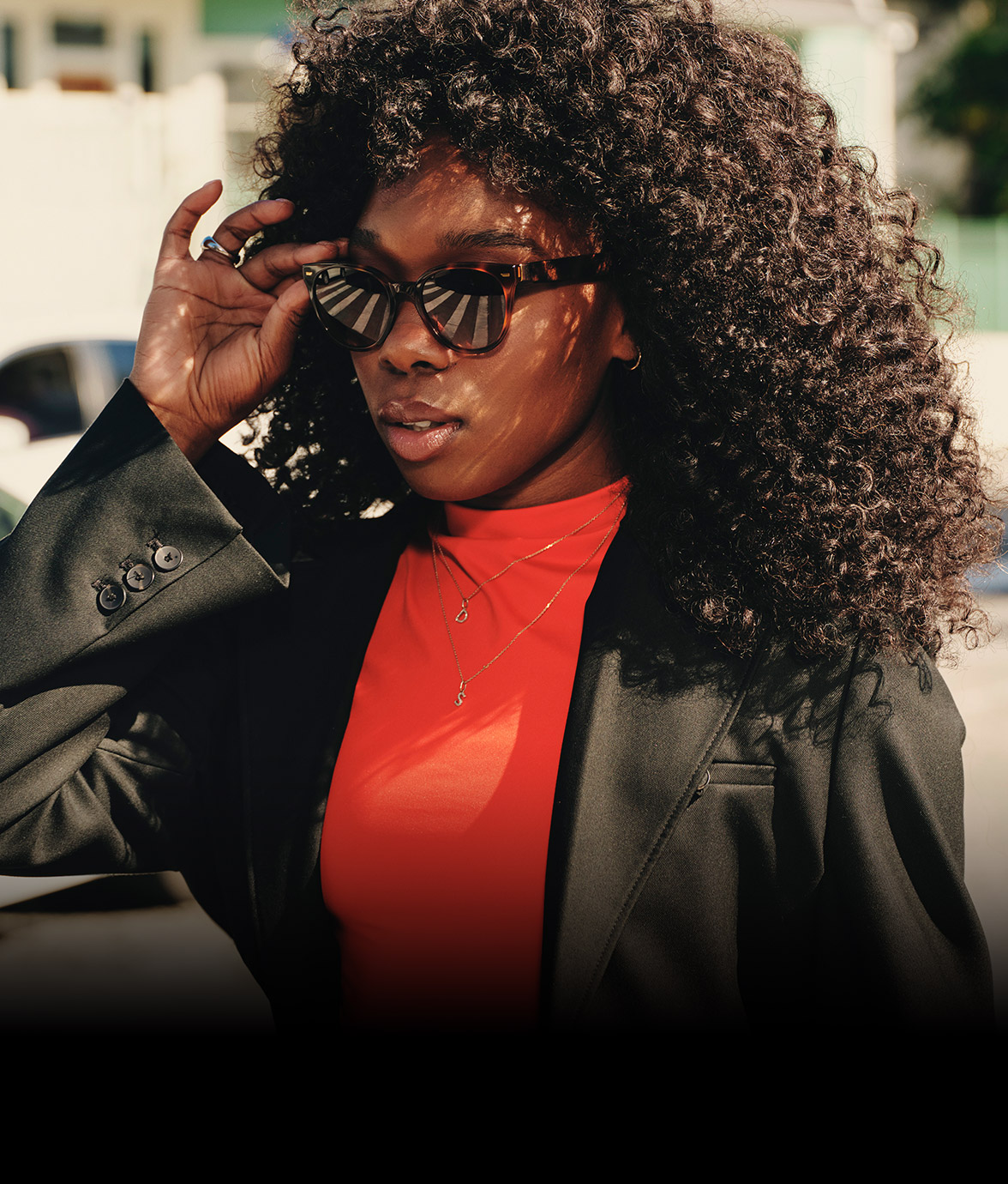 Person wearing Echo Frames smart audio glasses, adjusting them while dressed in a red top and black blazer outdoors with cars in the background.