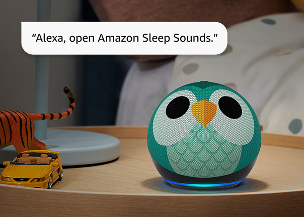 cho Dot 5th Gen in owl design with blue light ring on a wooden surface. Text reads: "Alexa, open Amazon Sleep Sounds." A toy tiger and yellow toy car visible nearby.