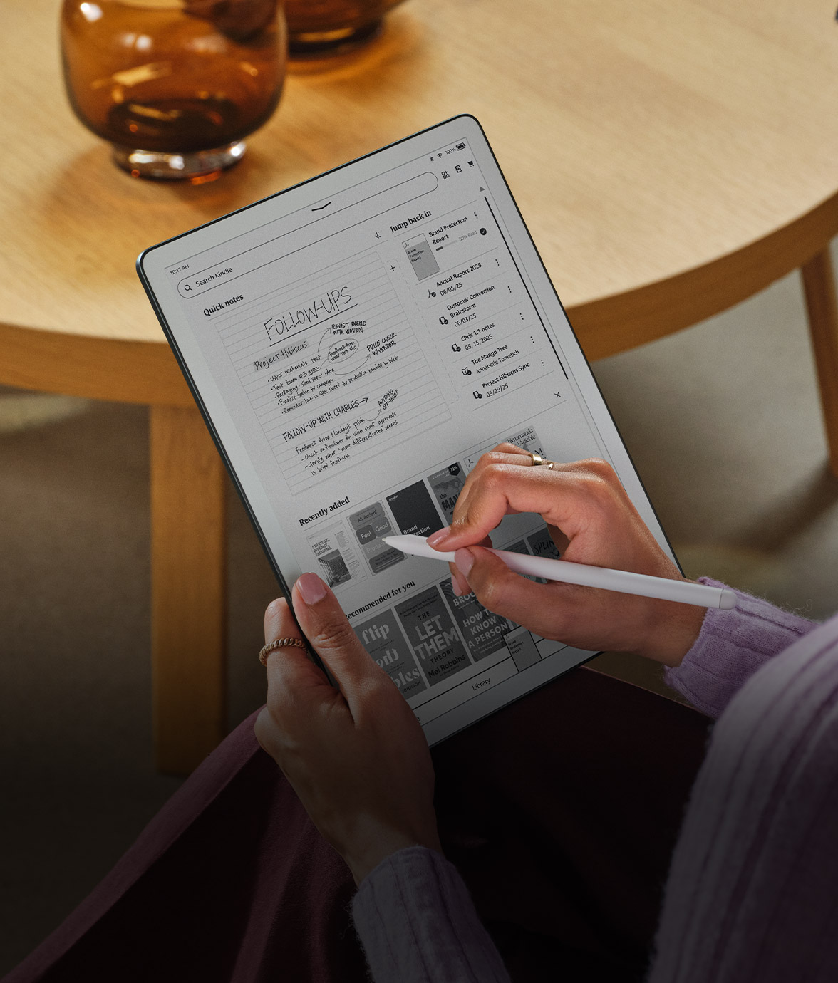 Person using Kindle Scribe without front light, screen showing home screen with books, notebooks, and folders.