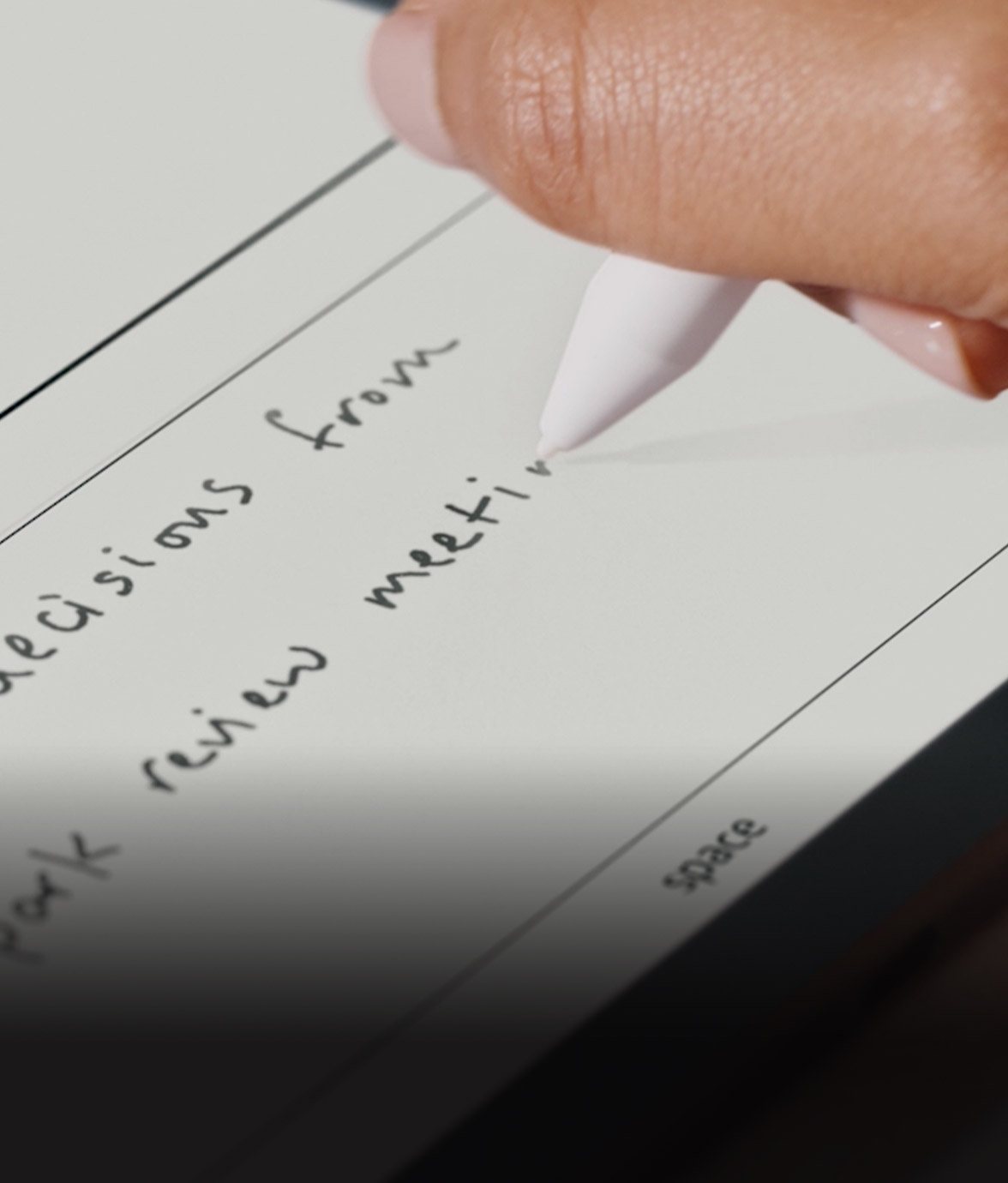 Close-up of a hand using the Kindle Scribe Colorsoft pen to write handwritten notes on the screen. The text reads part of a sentence including “decisions from … review meeting,” shown in black ink on a lined page template.