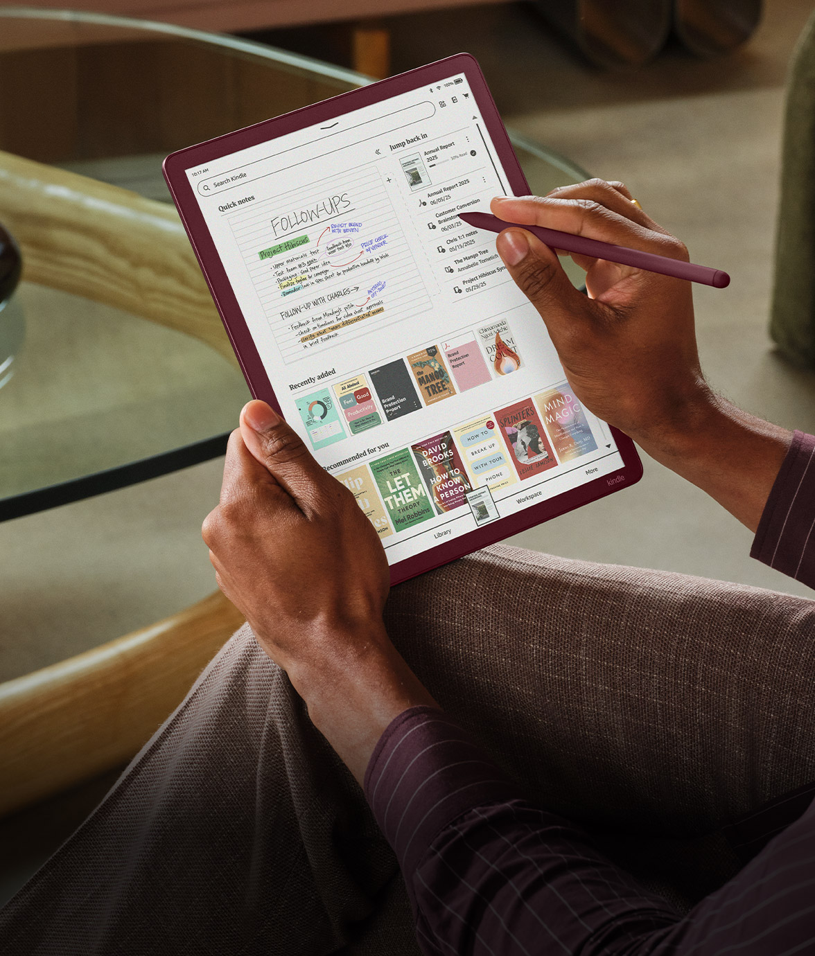 A hand holds a Kindle Scribe Colorsoft in portrait orientation. The home screen shows Quick Notes titled “Follow-Ups,” plus recent documents and a row of recommended book covers.