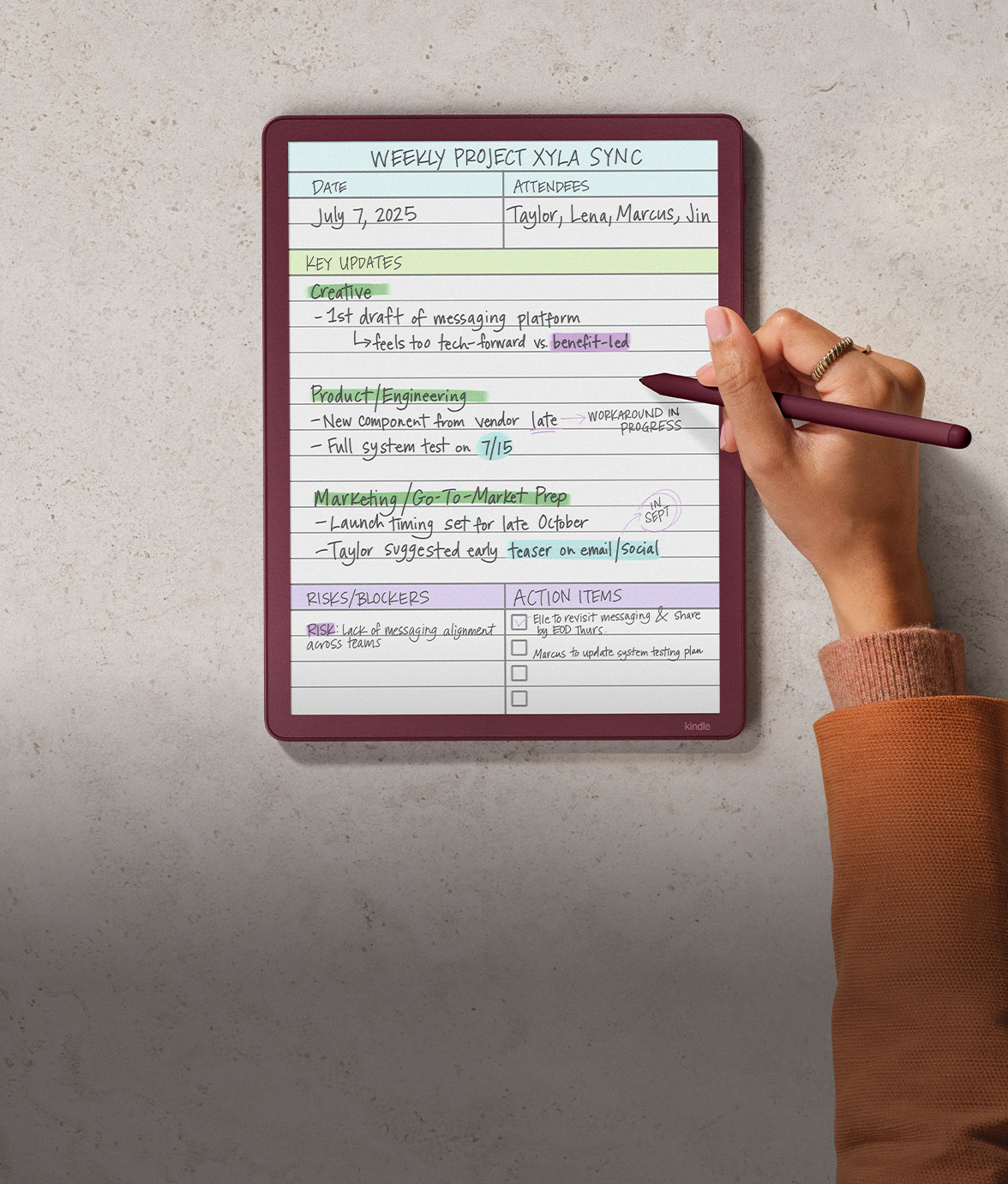 Kindle Scribe Colorsoft on a stone surface displaying handwritten notes titled “Weekly Project Xyla Sync.” Sections for updates, risks, and action items are visible, with purple handwriting and color highlights marking categories.