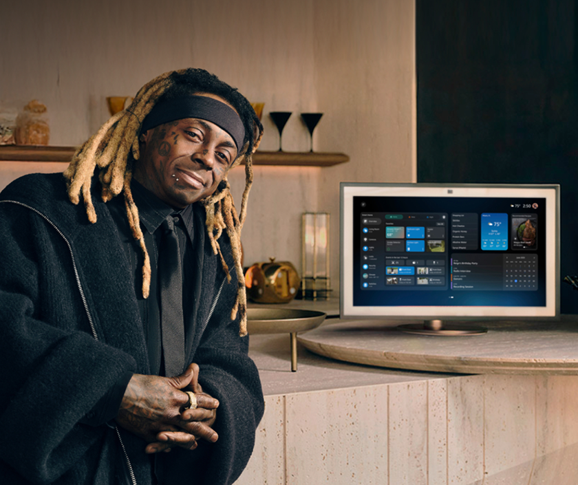 In a living room, a man leans against a counter next to an Echo Show 21 device.