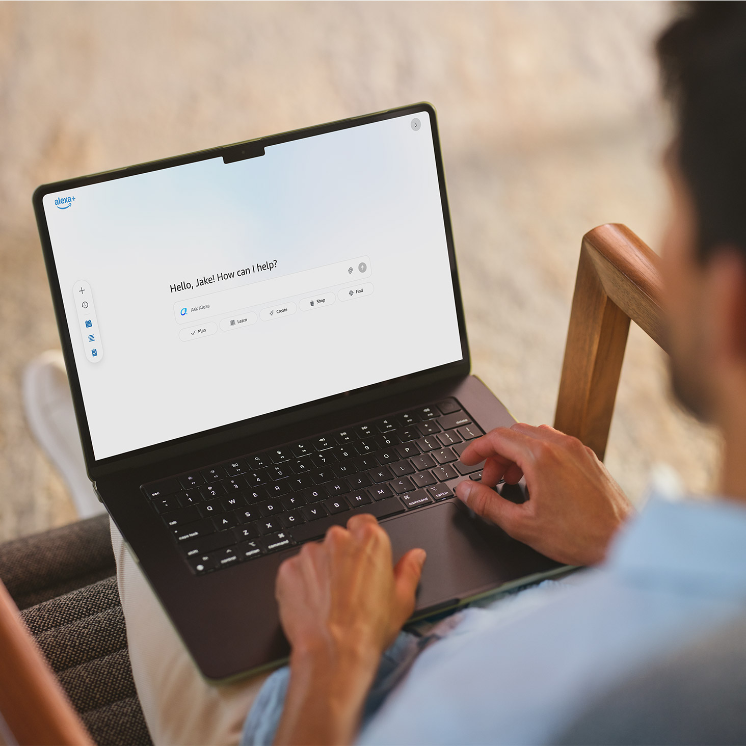 A man sits on a chair typing on a laptop. On display is [the] Alexa [on the web / website].