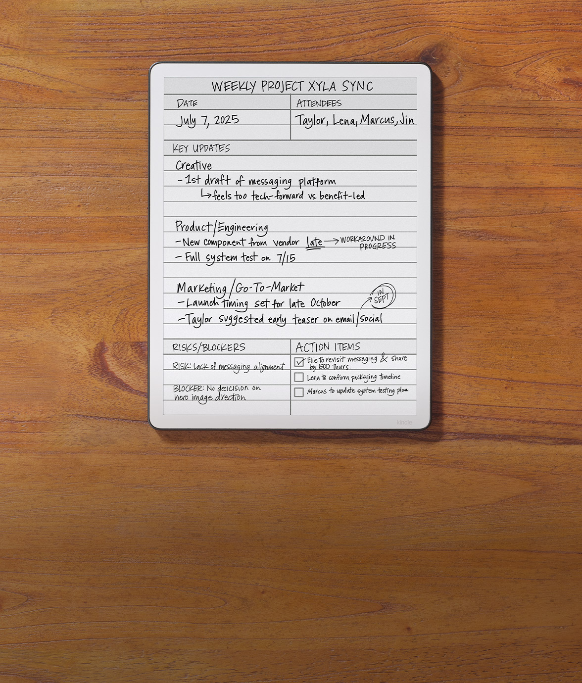 Kindle Scribe on a wooden surface, open to a digital notebook titled Weekly Project Xyla Sync. The page shows sections for updates, risks, and action items, combining printed text with handwritten notes.