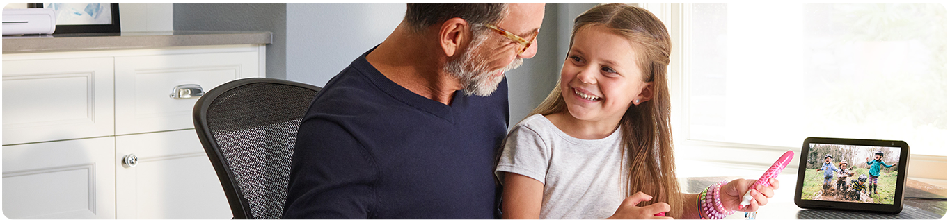 A man playing with a little girl by the window with an echo show device next to them. 