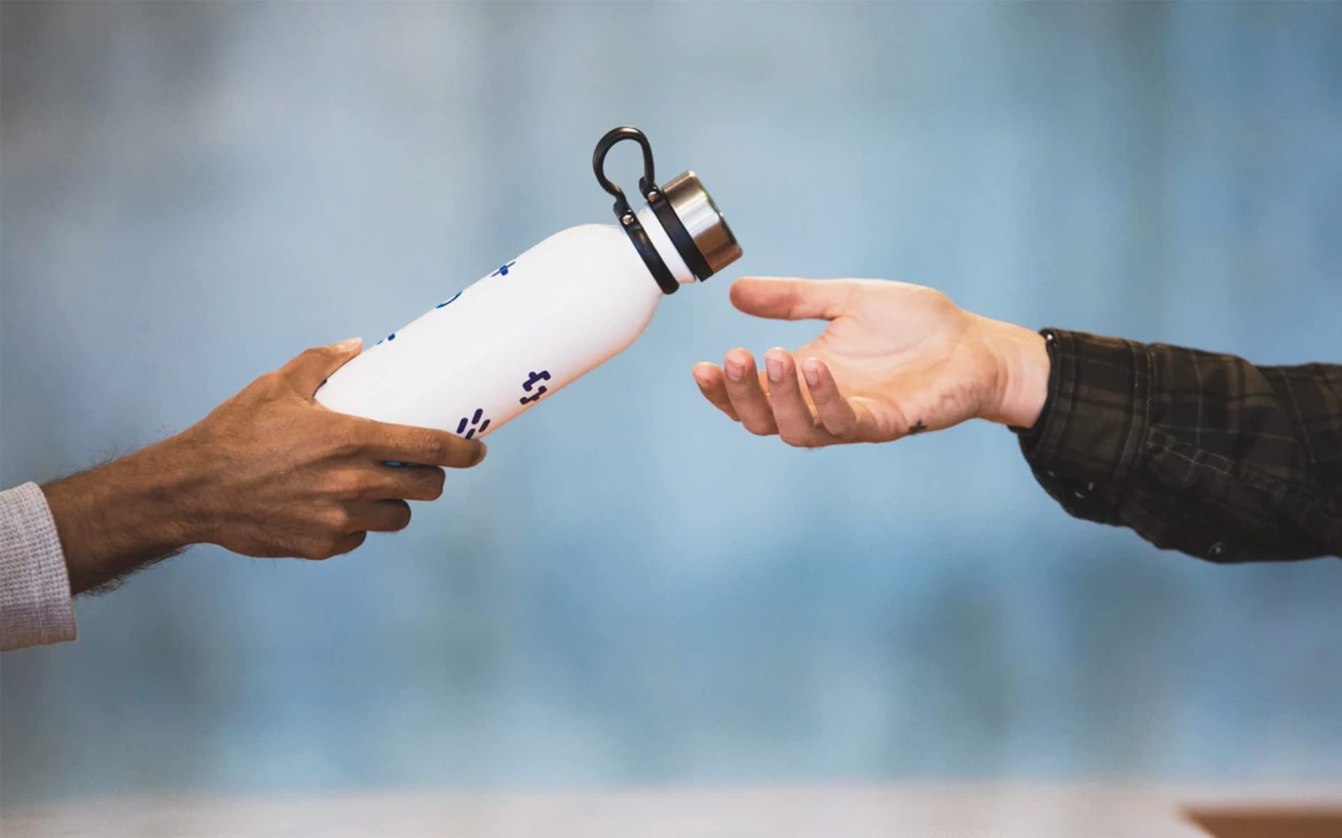 A hand passing a water bottle to another hand.