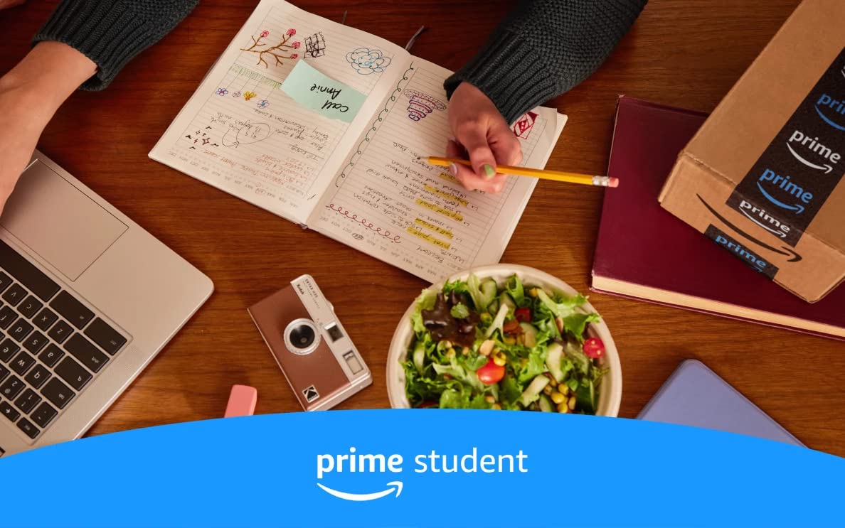 A person holding a pencil at a desk with a laptop, salad, and notebook on it.