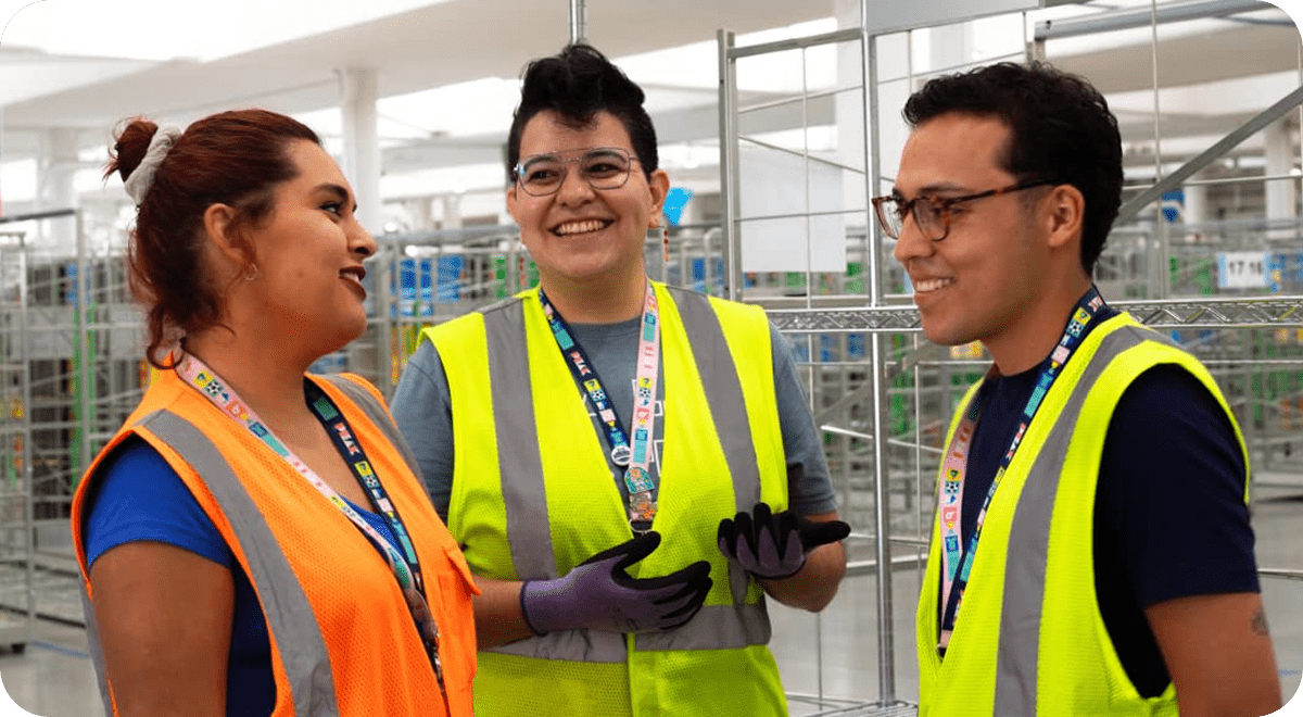 IMAGE – HERO Tres trabajadores con chalecos de seguridad conversando y sonriendo en un entorno de almacén.