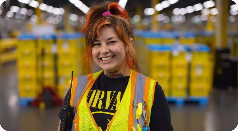 Amazon warehouse associate smiling at the camera on the warehouse floor with yellow storage totes behind