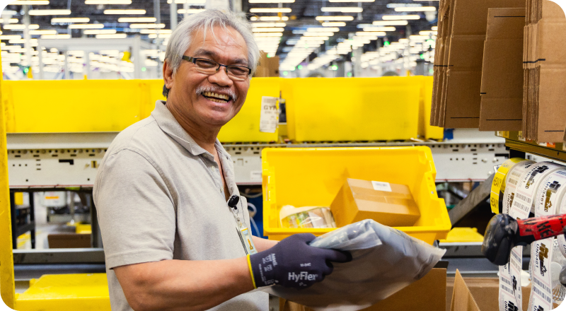 Amazon warehouse associate smiling while handling a package at a packing station