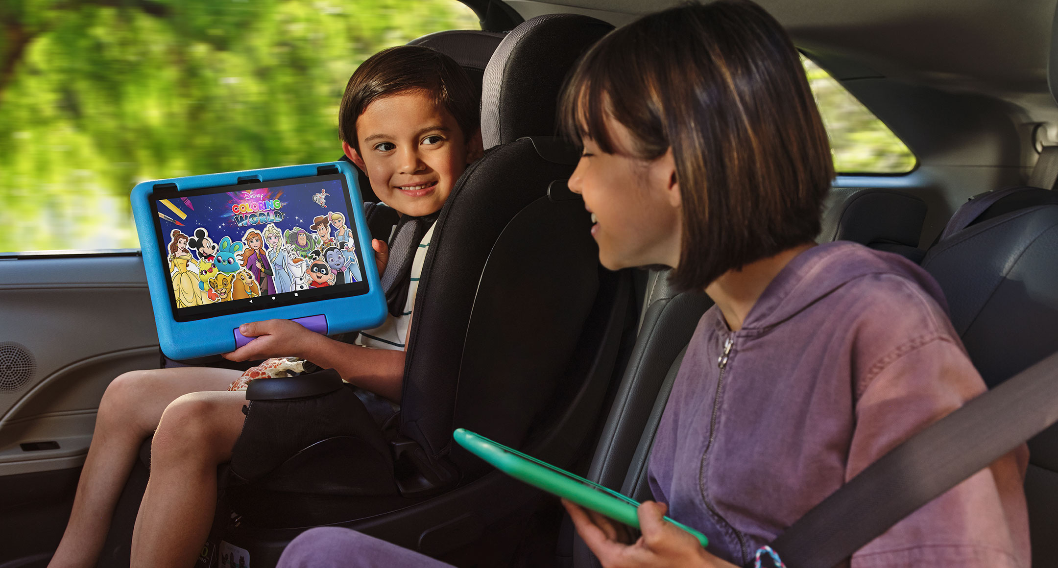 An older and a younger sibling sit in the back seat of a car, sharing content on their Fire HD 10 Kids tablets.