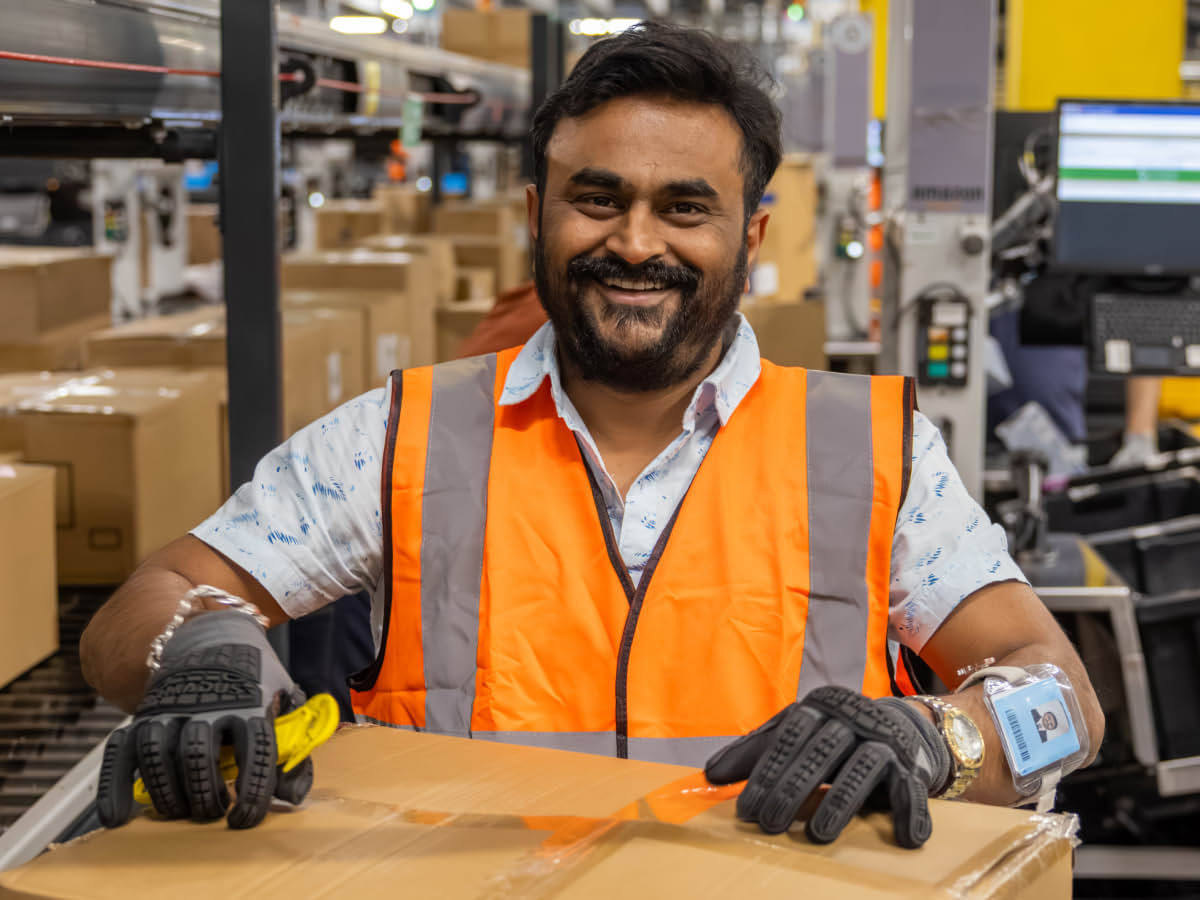 Amazon fulfillment center worker in orange safety vest at warehouse workstation