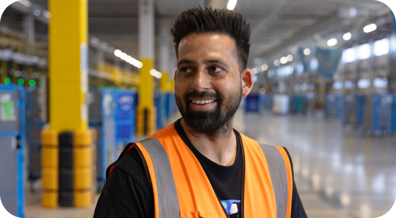 Amazon employee smiling in fulfillment center with storage shelves and totes in background