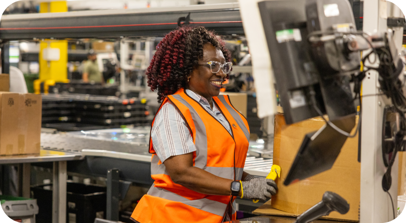Warehouse Associate smiling while operating equipment at Amazon fulfillment center workstation