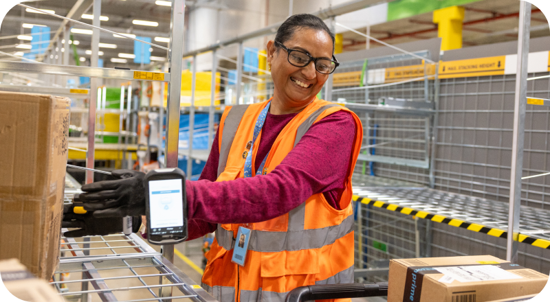 Female associate in the warehouse working and smiling while wearing a safety vest.