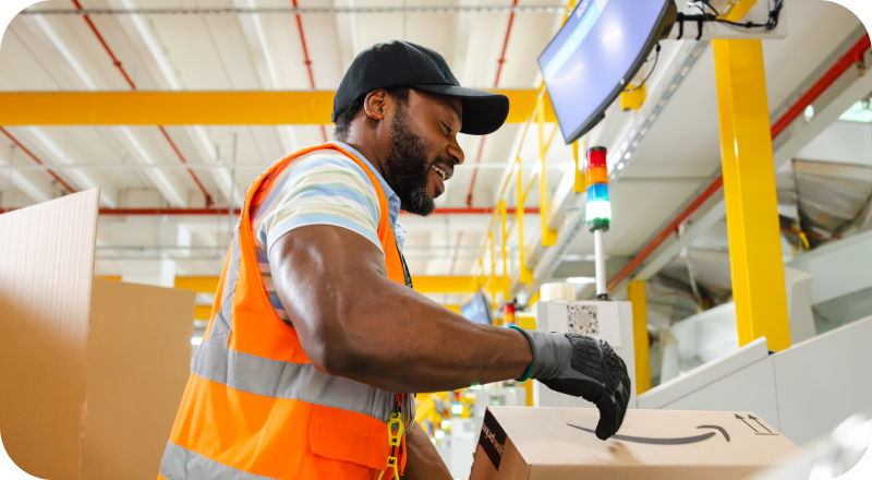 Male associate in the warehouse working and smiling while wearing a safety vest.