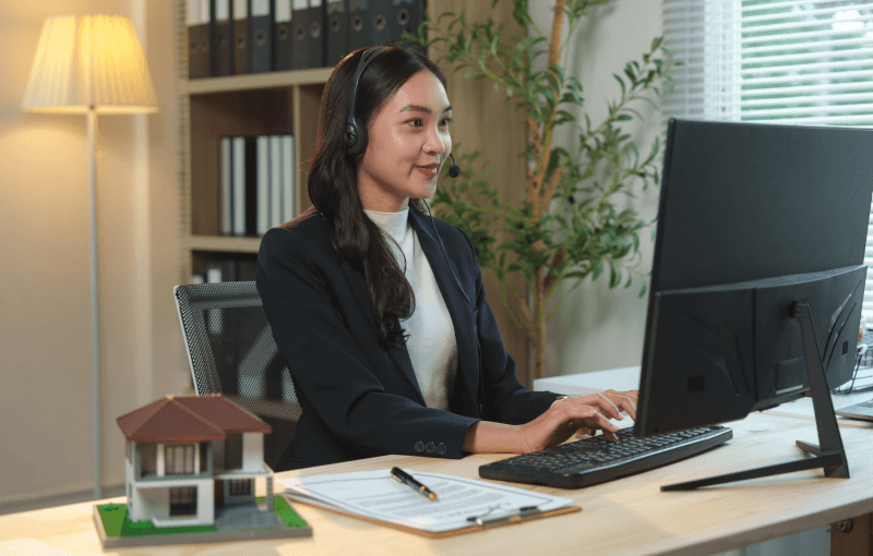 A customer service representative wearing glasses and a headset smiles while working on a desktop.