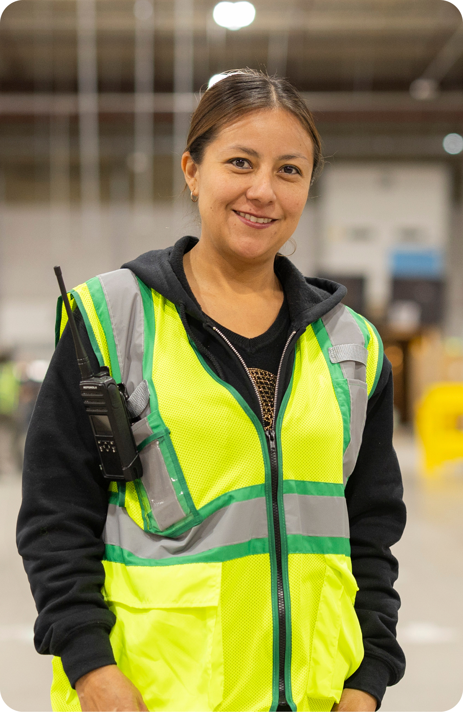 Associate in safety vest with radio smiles at camera in fulfillment center