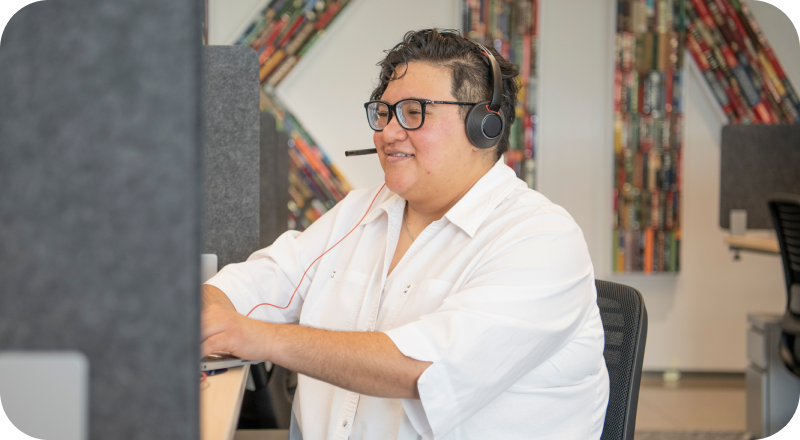 Person with glasses and headset smiles while working at computer desk