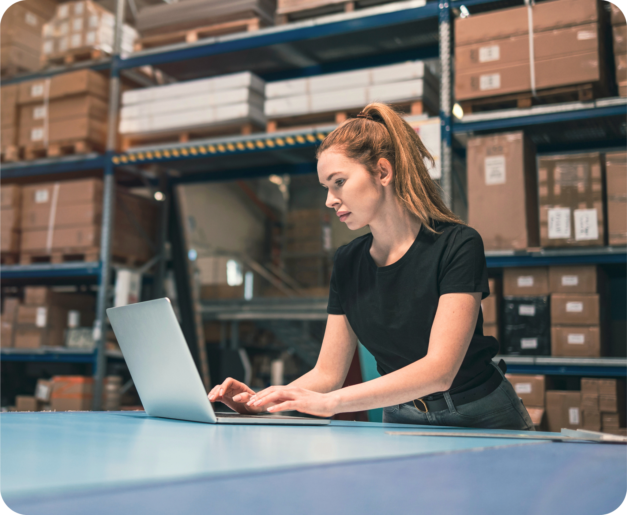 Profissional de logística gerenciando estoque com computador em centro de distribuição.