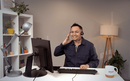Um associado de atendimento ao cliente, usando headset, sorri enquanto trabalha no computador.