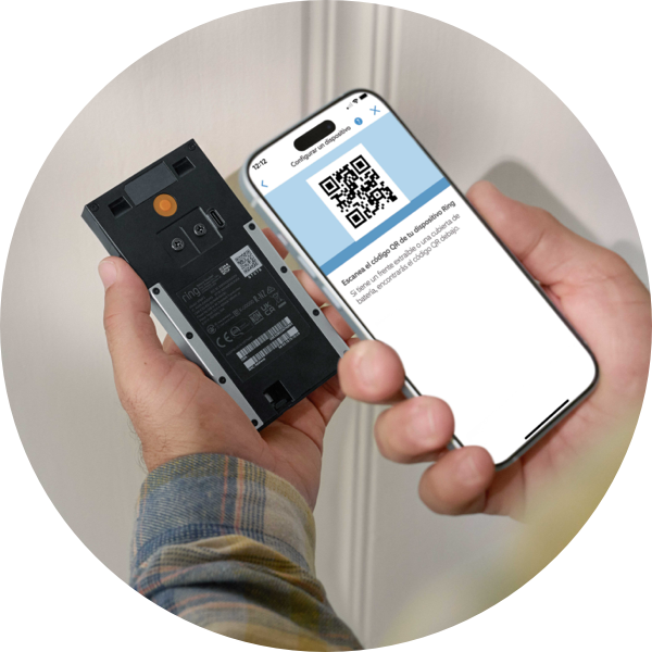Un par de manos sostienen un teléfono y un Timbre con cámara inalámbrico Ring. La pantalla del teléfono muestra un código QR e indica al usuario que debe escanear el código QR de la parte posterior de su dispositivo.