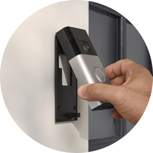 Una mano fija el Timbre con cámara inalámbrico Ring a un soporte instalado al lado de una puerta principal.