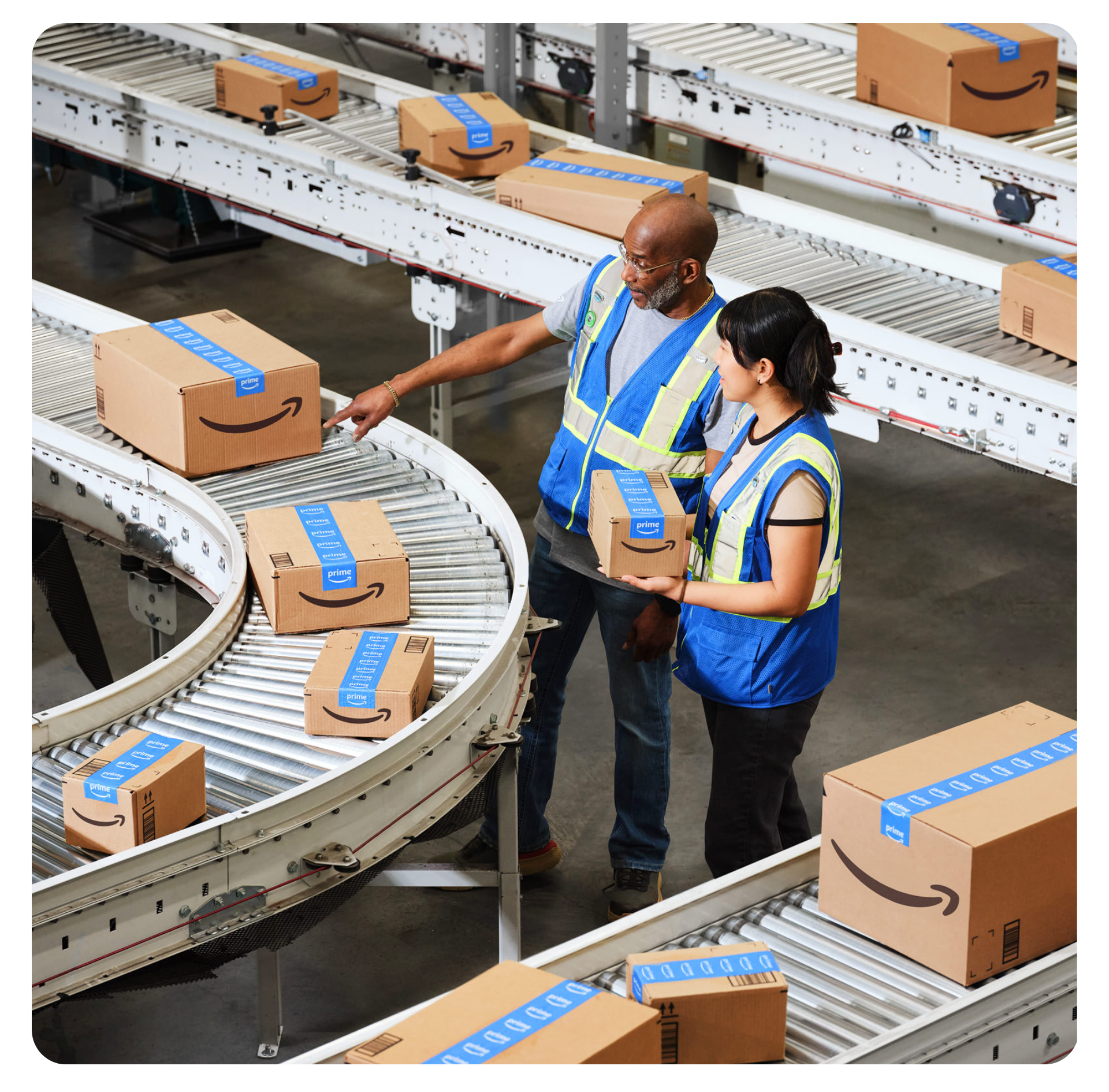 Dois funcionários com coletes em centro de distribuição com esteiras e caixas com logo Amazon
