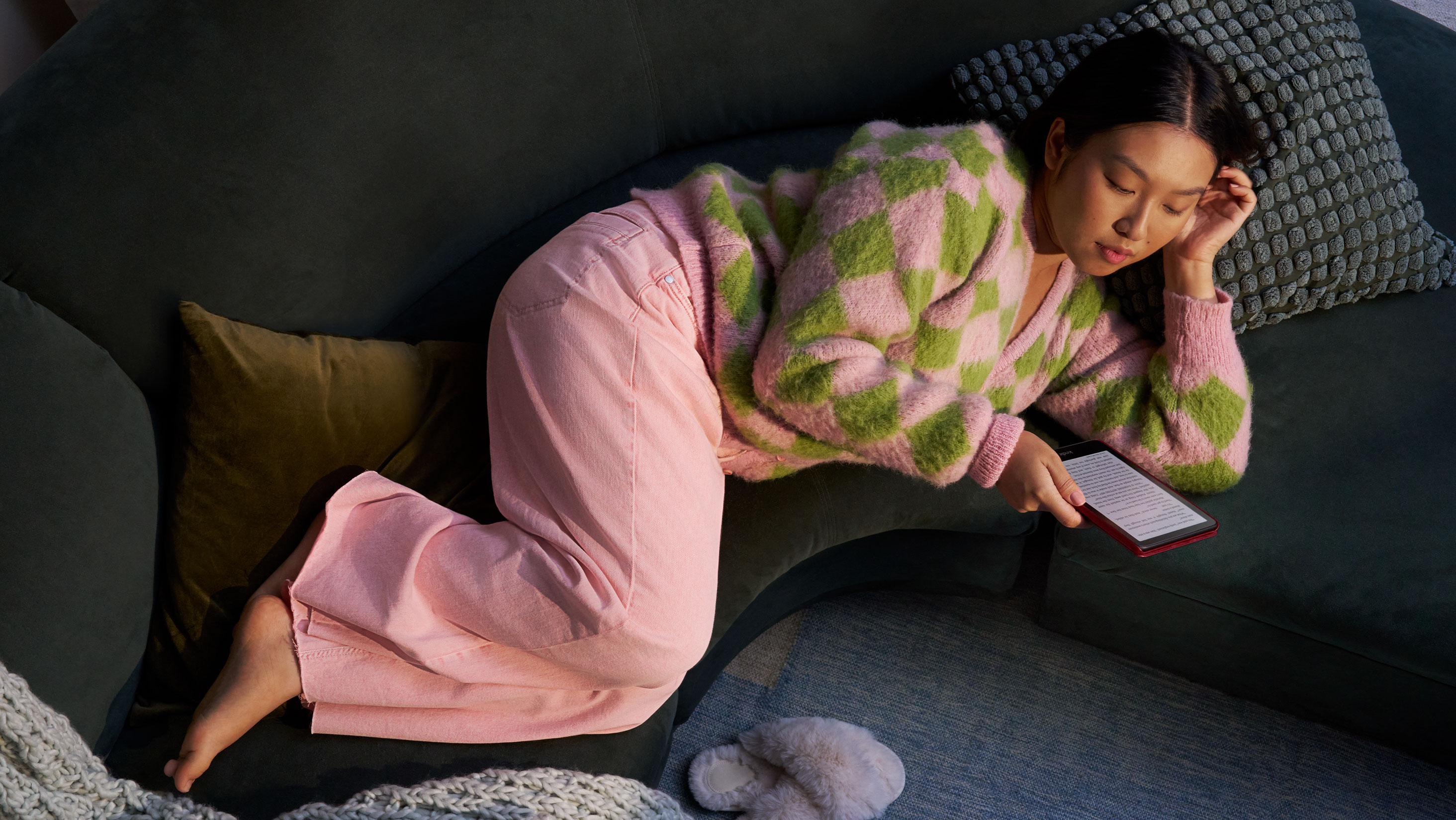 A woman lays on a couch while reading her Kindle Paperwhite Signature Edition.