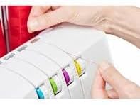 Close-up of hands threading the SINGER SE017 Elite Serger, focusing on the tension dials and thread paths.