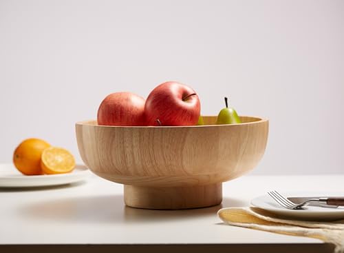 Natural wooden bowl filled with green apples, a pear, and oranges on a wood table