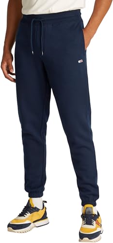 Modelo masculino viste pantalones de chándal Tommy Jeans en color azul marino en vista lateral con zapatillas deportivas