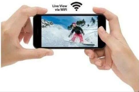 Hands holding a smartphone displaying a live view from the action camera, showing a person snowboarding.