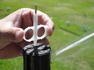 Hand using Hunter adjustment tool on a sprinkler head with water spraying