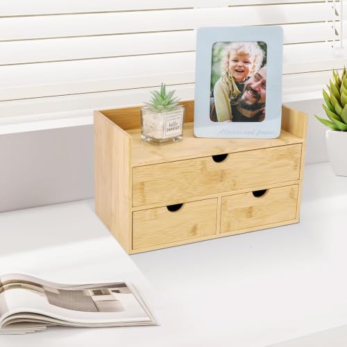 Light bamboo desktop organizer with three drawers, an open upper shelf, a framed photo, and a small plant on a white desk near a window.