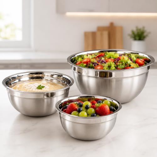 Conjunto de três tigelas de aço inoxidável de tamanhos diferentes dispostas sobre uma bancada de cozinha, com uma tigela contendo salada, outra com uma mistura cremosa e a menor com frutas frescas.