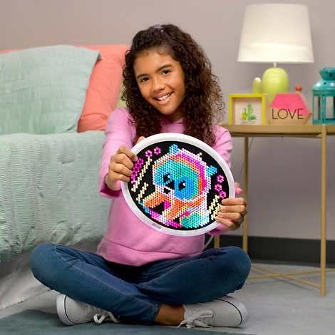 A girl sitting on the floor, holding an illuminated Lite Brite Oval HD Deluxe unit with a colorful animal design.