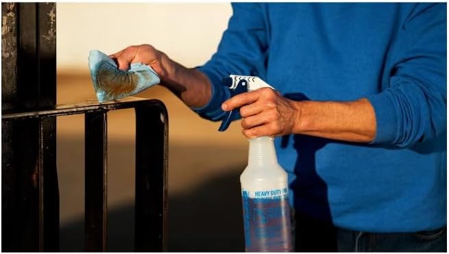 Person cleaning a greasy metal surface with a spray bottle and cloth