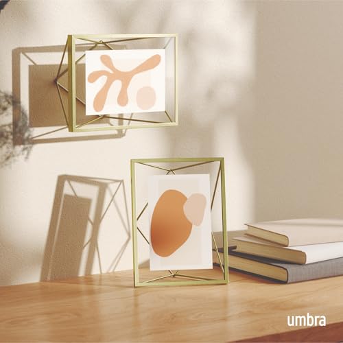 Two gold geometric picture frames displaying abstract prints on a wooden surface.