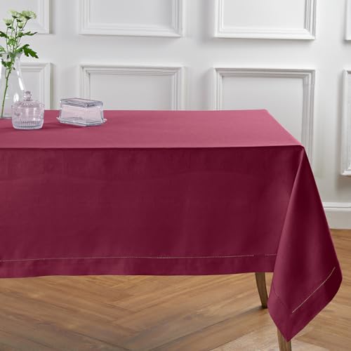 Deep red linen tablecloth on a rectangular dining table with small glass containers and a clear vase