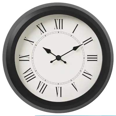 Ikea wall clock mounted on a white wall, next to a lamp and a vase with flowers.